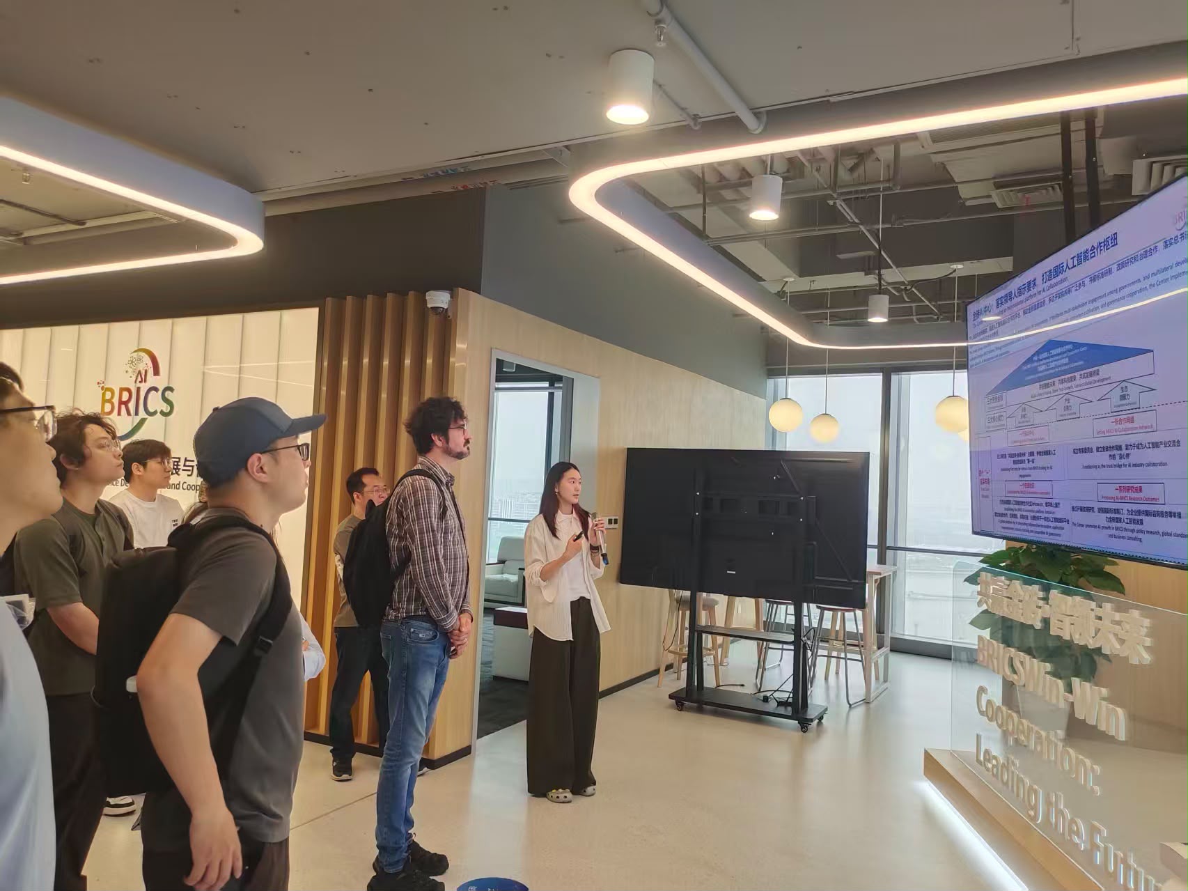 A centre representative presenting the BRICS AI cooperation framework on a large screen, with the group looking on