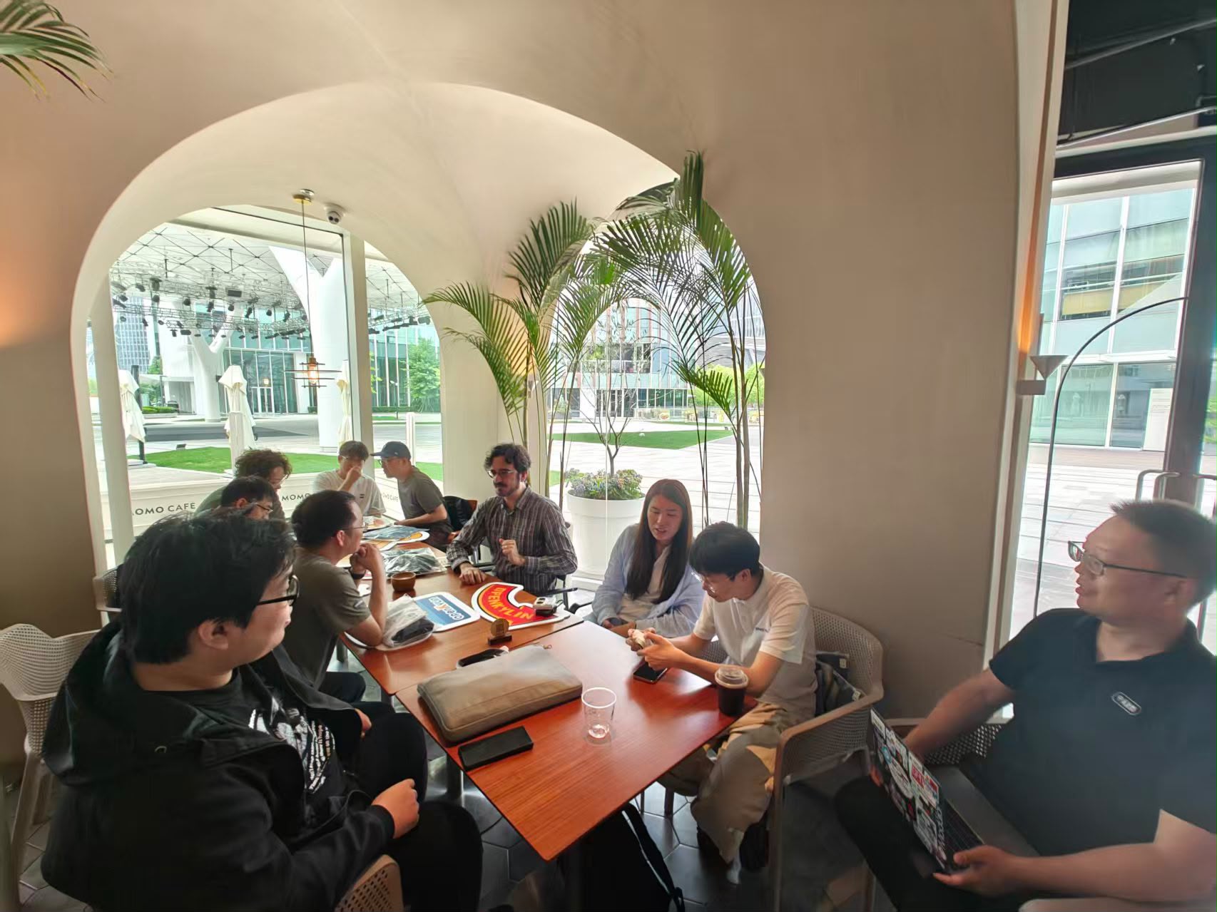 The group gathered around a table at MoMo Cafe, with KDE materials visible and the arched windows looking out onto the plaza