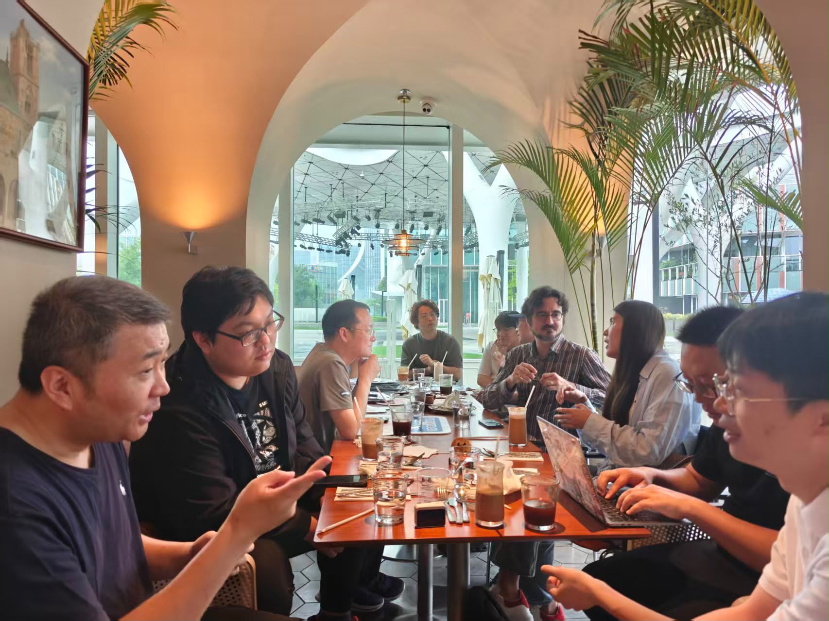 The full group deep in conversation at MoMo Cafe, laptops and drinks spread across the table